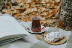 A warm autumn picnic featuring a glass of tea, a pastry, and an open book on a blanket.