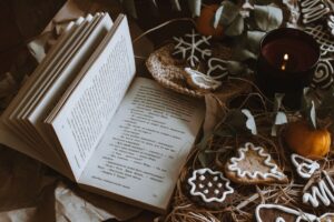 Open book surrounded by festive gingerbread cookies, candle, and decorations in a cozy setting.