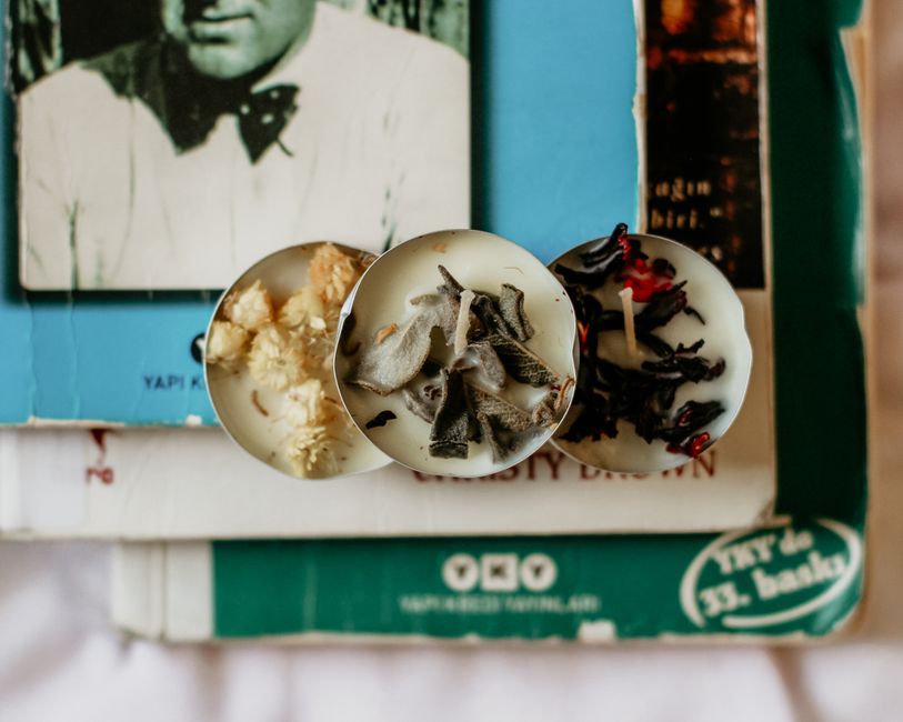 Three aromatic wax candles with herbs placed on vintage books for a cozy atmosphere.