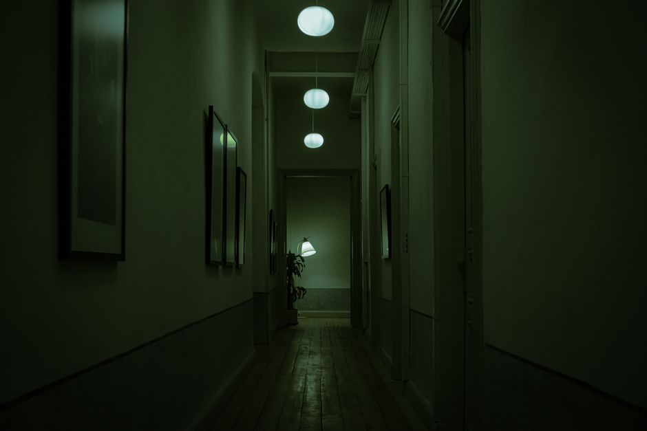 Explore the moody atmosphere of a narrow corridor with green lighting and hanging lamps.