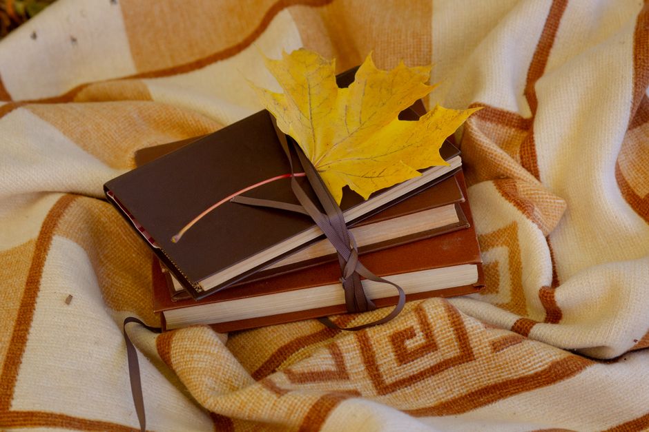 Autumn still life with books, a maple leaf, and a cozy blanket.