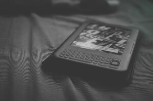Black and white e-reader resting on patterned bedding, focusing on technology and reading.