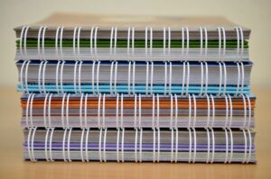 A stack of colorful spiral-bound notebooks placed on a wooden table, showcasing various colors and designs.