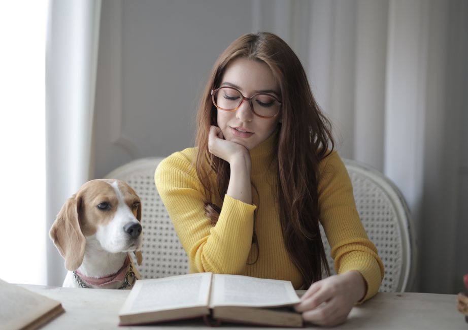Young woman reading a book with her dog beside her indoors.